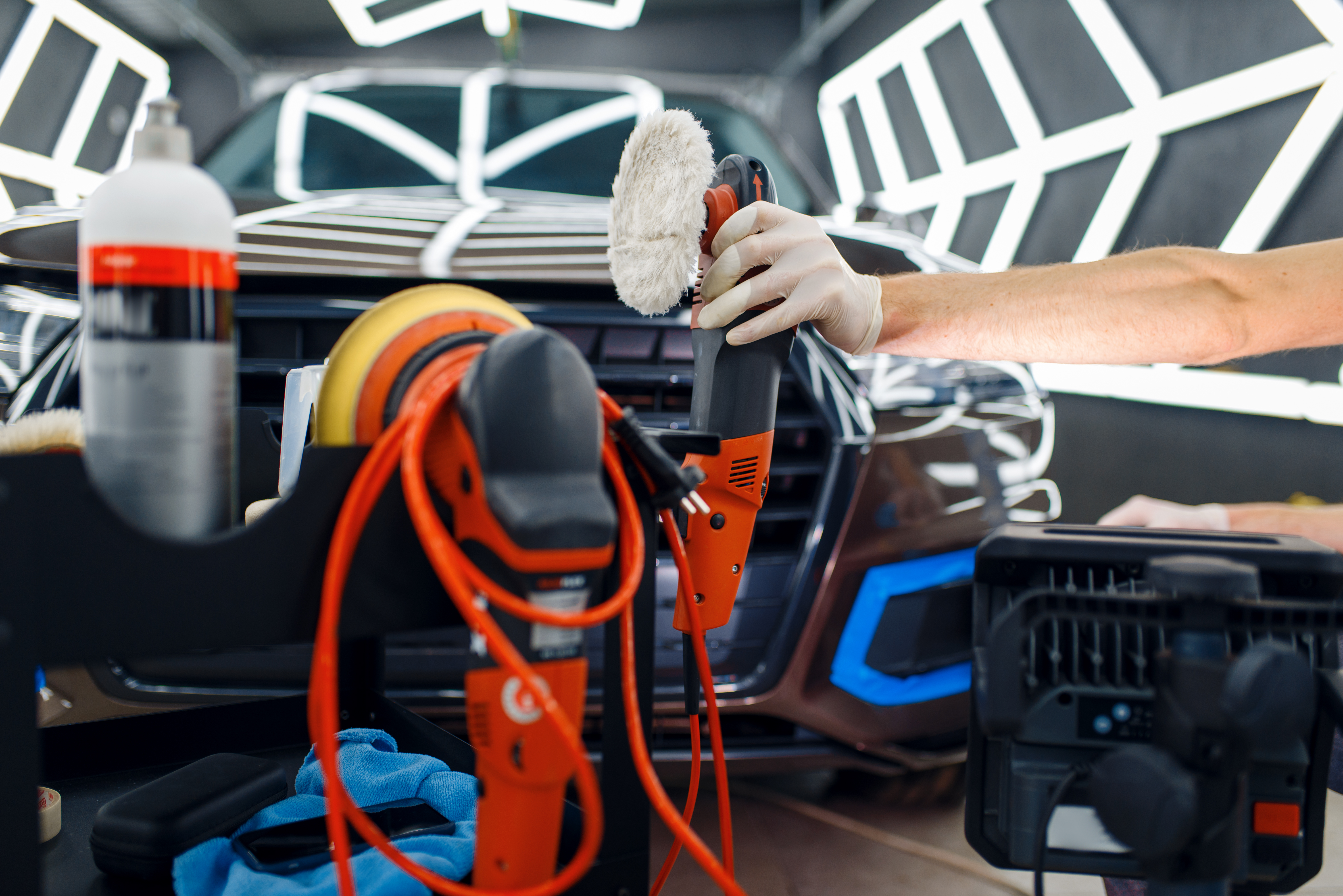 Male worker near toolbox with polishing machine and polish tools, car detailing. Preparationa before installation of coating that protects the paint of automobile from scratches, auto tuning